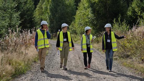 Four people wearing safety vests walking down a gravel road