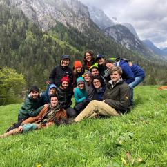 A group of students sitting on a hillside in Bavaria, with mountsins in the backgroud