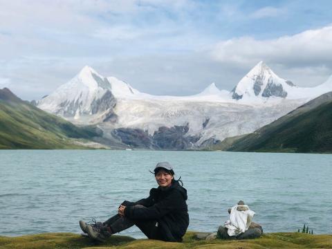 Irene Shi sitting in front of blue-green lake in the mountains